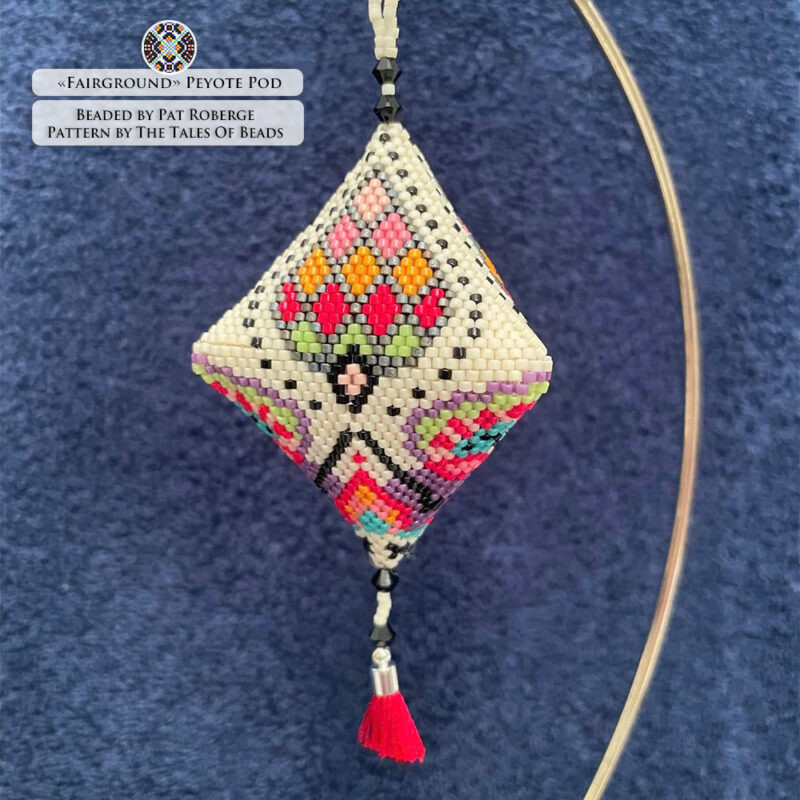 Close-up of the beaded pod ornament with a vibrant repetitive motif on a cream background displayed on plain blue background