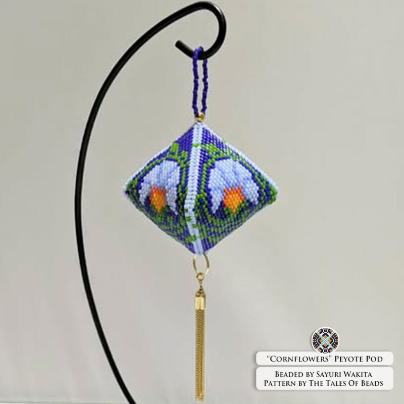 Peyote pod beaded ornament with a blue floral design hanging on a stand against a white background