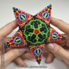 A beaded star with a repetitive botanic motif held in hands for scale