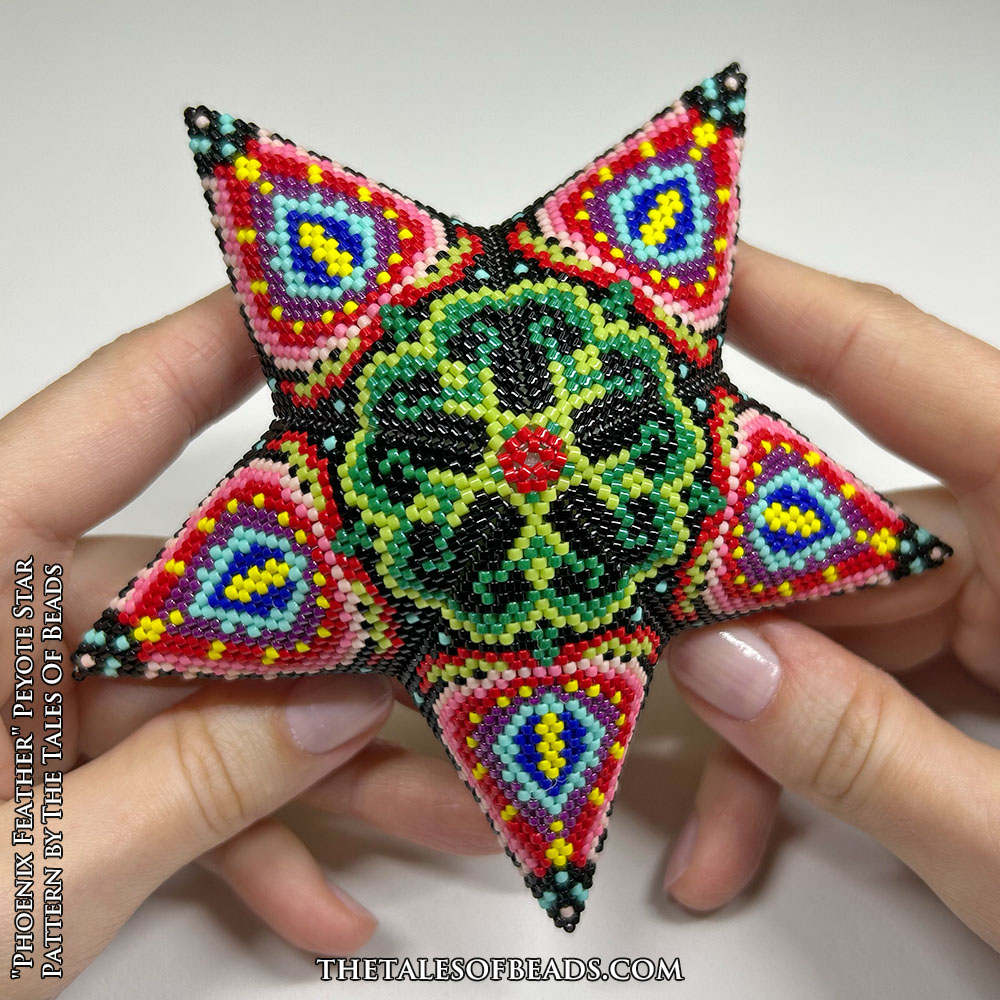 A beaded star with a repetitive botanic motif held in hands for scale