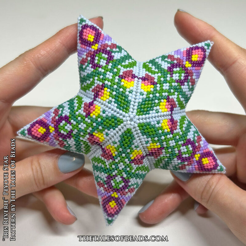 A beaded star with a repetitive botanic motif held in hands for scale