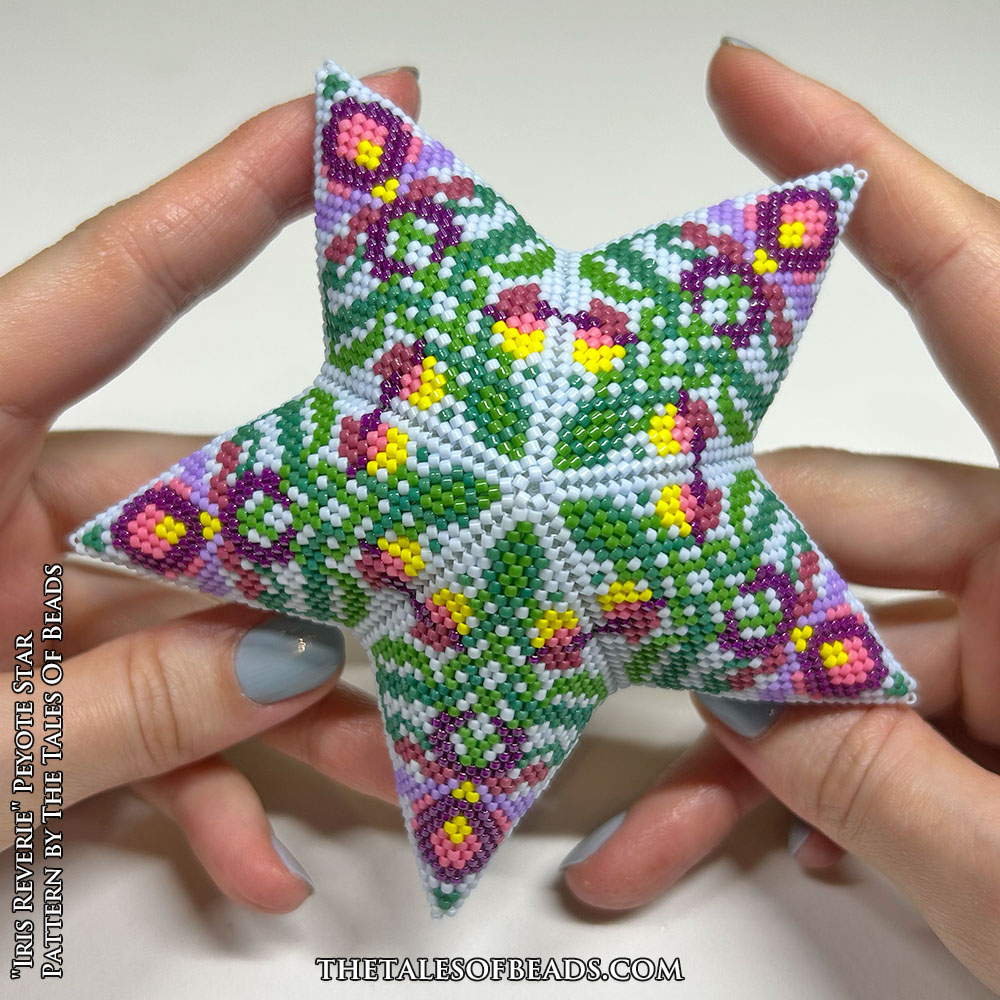 A beaded star with a repetitive botanic motif held in hands for scale